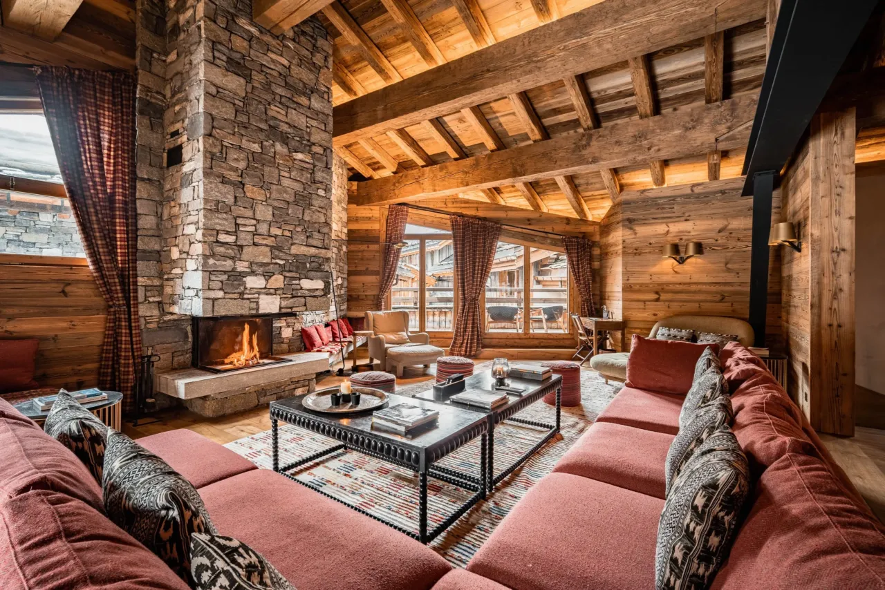 Salon chalet avec chemin&eacute;e en pierres et canap&eacute; rouge, dans&nbsp;un chalet&nbsp;&agrave; Val d&rsquo;Is&egrave;re, H&ocirc;tel Village La Mourra.