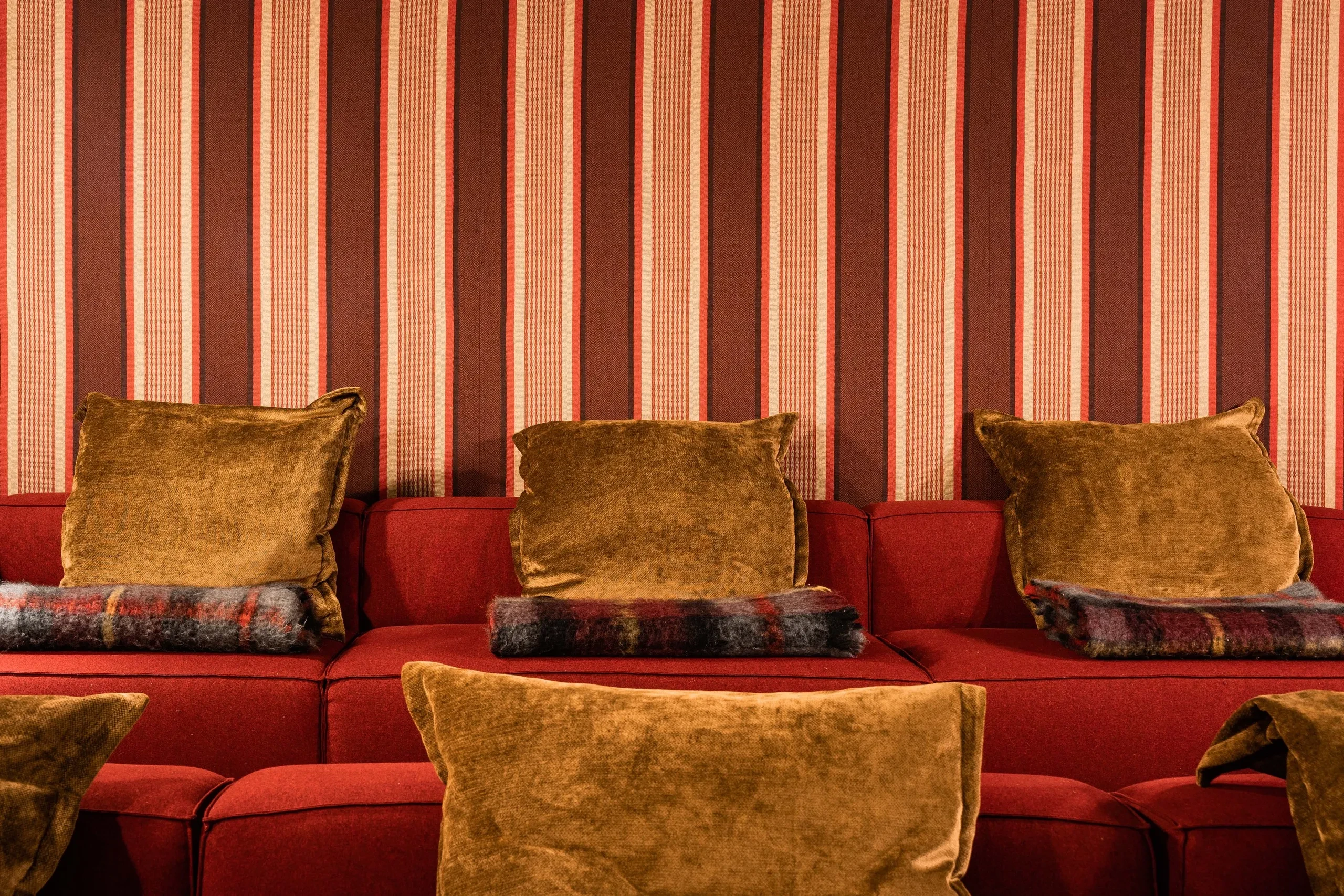 Canapés rouges avec coussins marron et rayures murales, à Val d’Isère, Hôtel Village La Mourra.